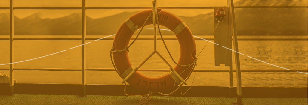 Foto com um filtro amarelo de uma boia de salva-vidas laranja e branca, amarrada a uma grade de proteção de um barco. Ao fundo o mar e algumas montanhas